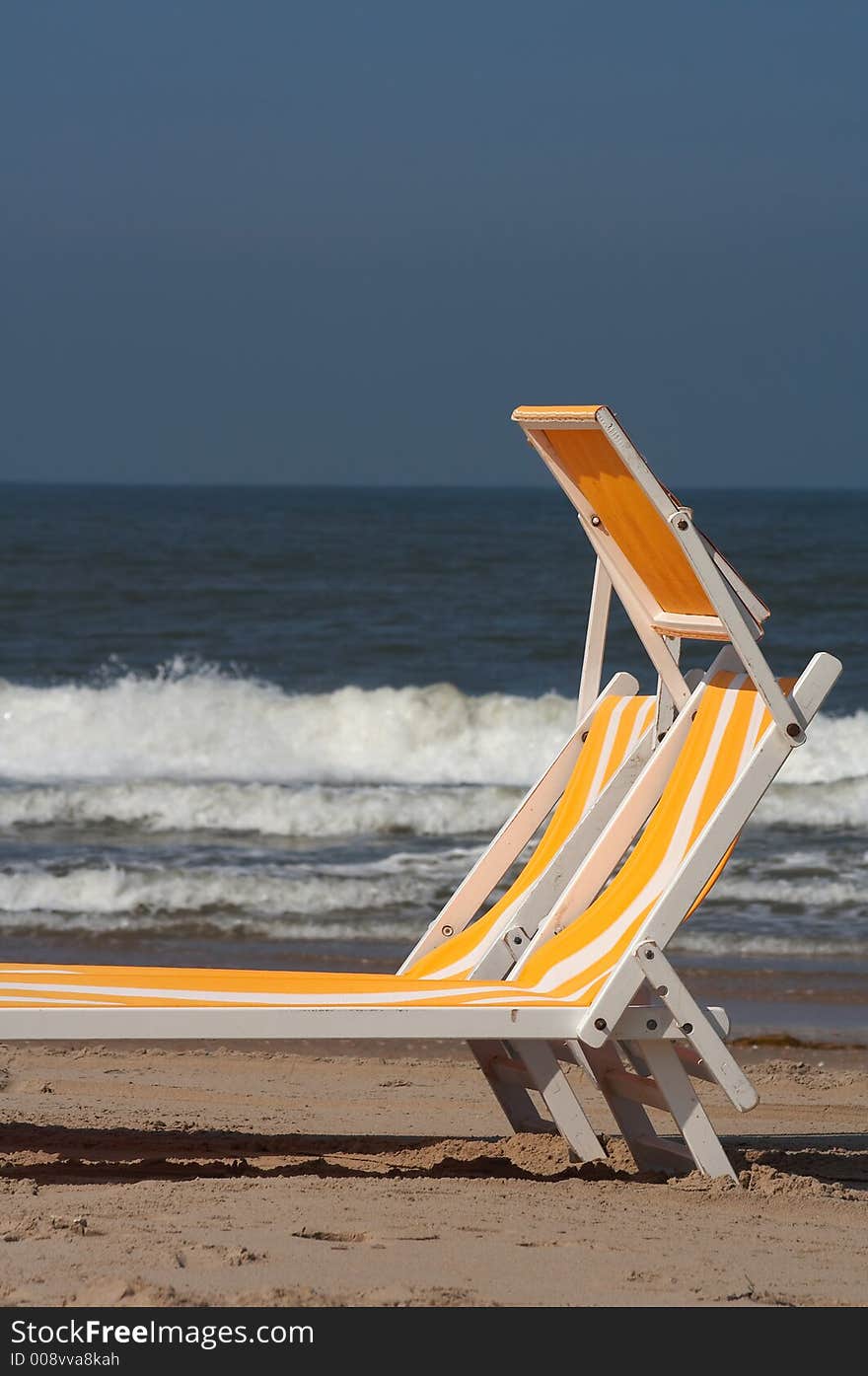 Two beach chairs in the sand with the sea/ocean on the background, plenty of copyspace. Two beach chairs in the sand with the sea/ocean on the background, plenty of copyspace