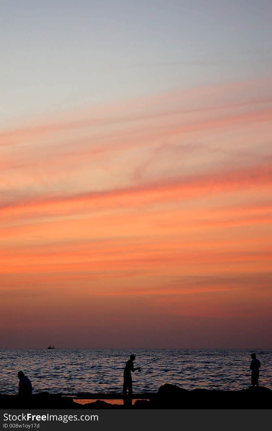 A group of fisherman pictured while fishing at the sea side during sunset.