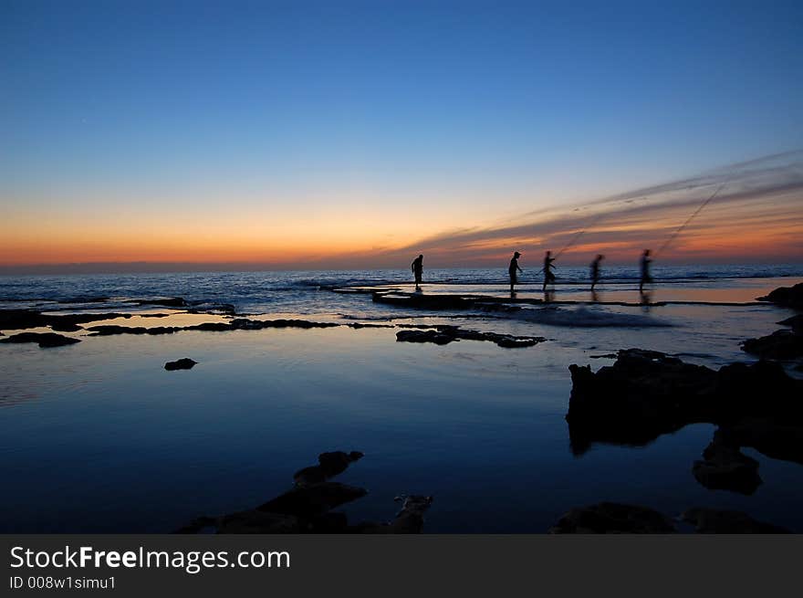 A group of fisherman pictured walking after fishing at the sea side during sunset. A group of fisherman pictured walking after fishing at the sea side during sunset.