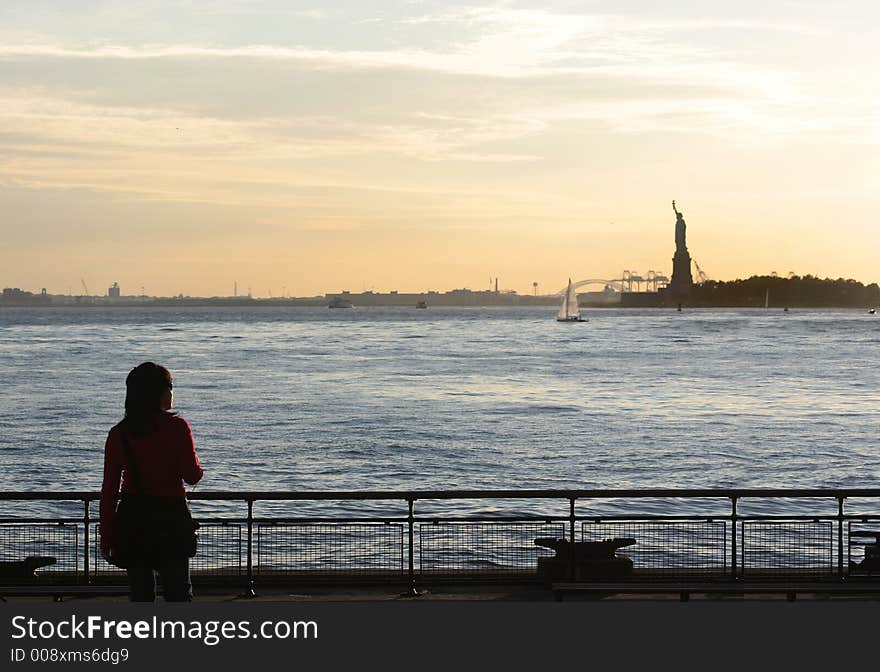 Scenic view from of the Statue of Liberty from Battery Park with young Asian woman looking on. Scenic view from of the Statue of Liberty from Battery Park with young Asian woman looking on