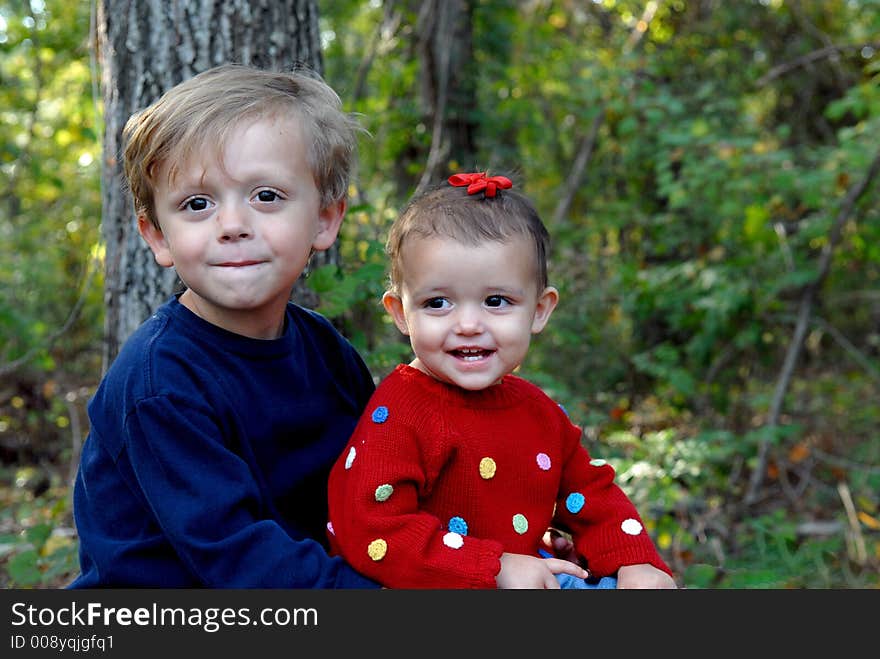 A little girl smiling and a young boy looking with a little smile in an outdoor setting. A little girl smiling and a young boy looking with a little smile in an outdoor setting.