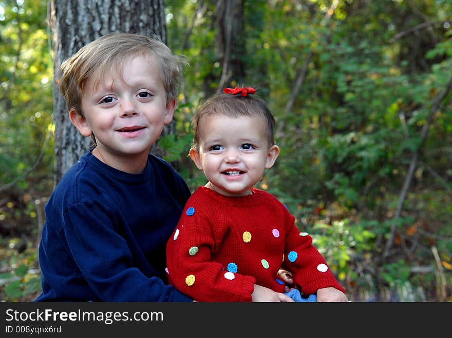 A little girl smiling and a young boy looking with a little smile in an outdoor setting. A little girl smiling and a young boy looking with a little smile in an outdoor setting.