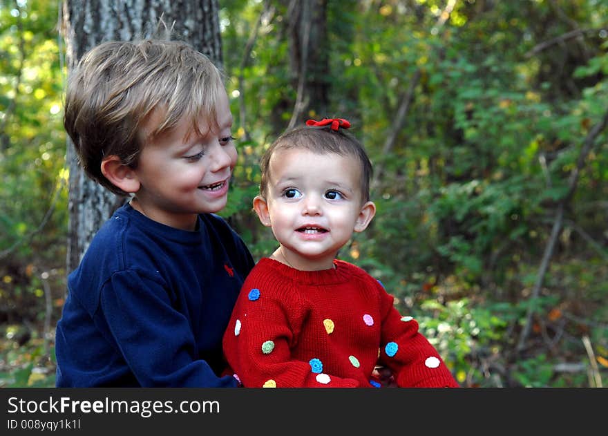 A little girl smiling and a young boy looking at her  in an outdoor setting. A little girl smiling and a young boy looking at her  in an outdoor setting.