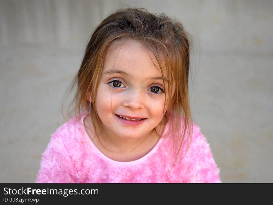 A pretty little girl dressed in a fuzzy pink shirt with a sweet smile and big brown eyes.