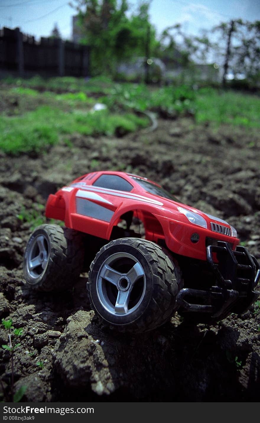 Toy off-road car on ground overcoming obstacle, with slight vignette and perspective. Film scan.
