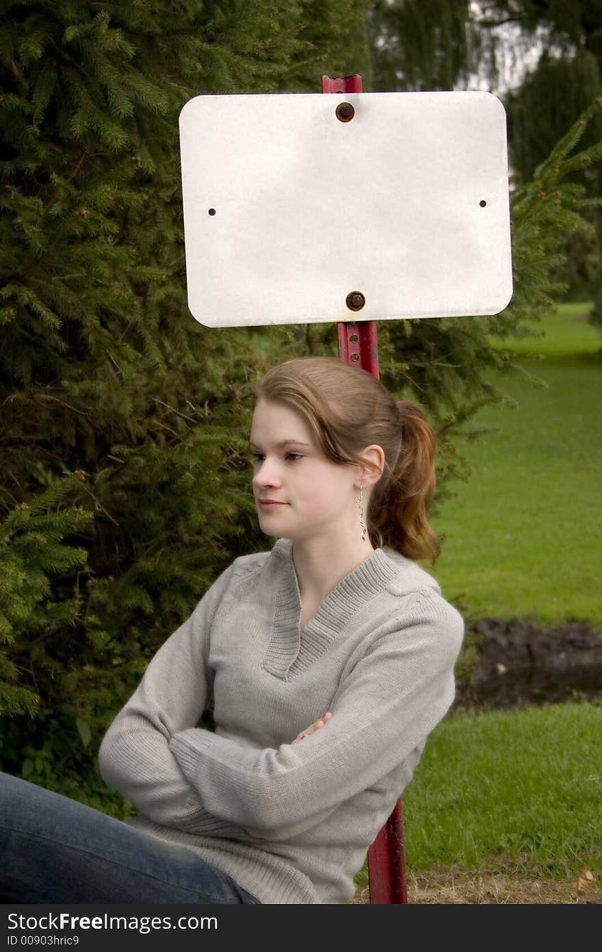 Attractive teen leaning up against a blank sign in a park setting. Attractive teen leaning up against a blank sign in a park setting.