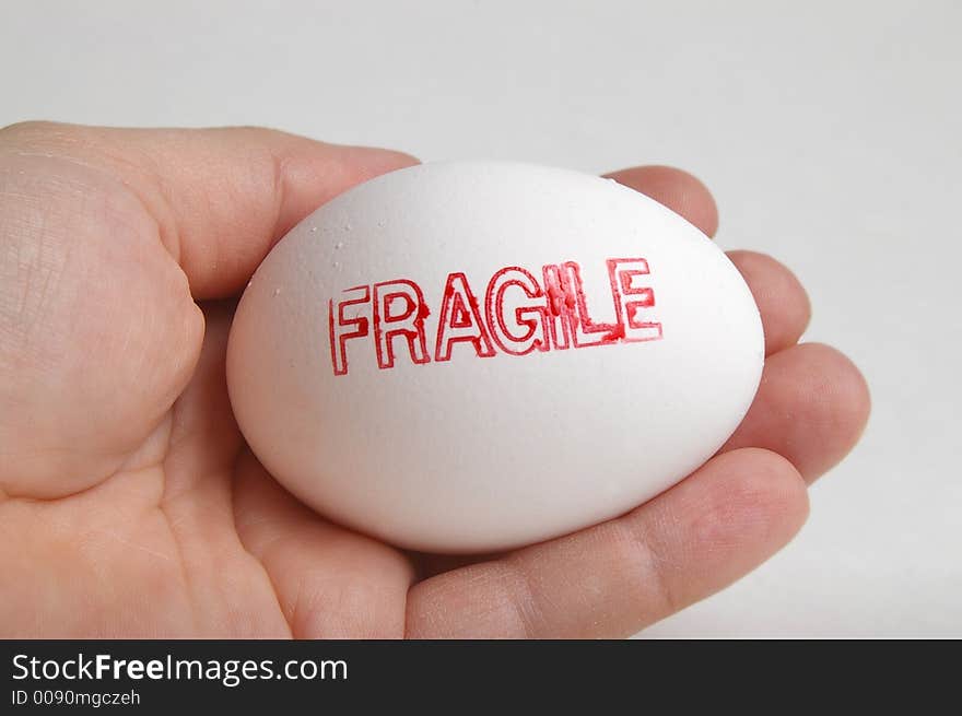 Hand holding a white egg that is stamped fragile. Hand holding a white egg that is stamped fragile.