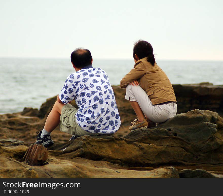 A couple on the shore watching the waves crash against the rocks. A couple on the shore watching the waves crash against the rocks.