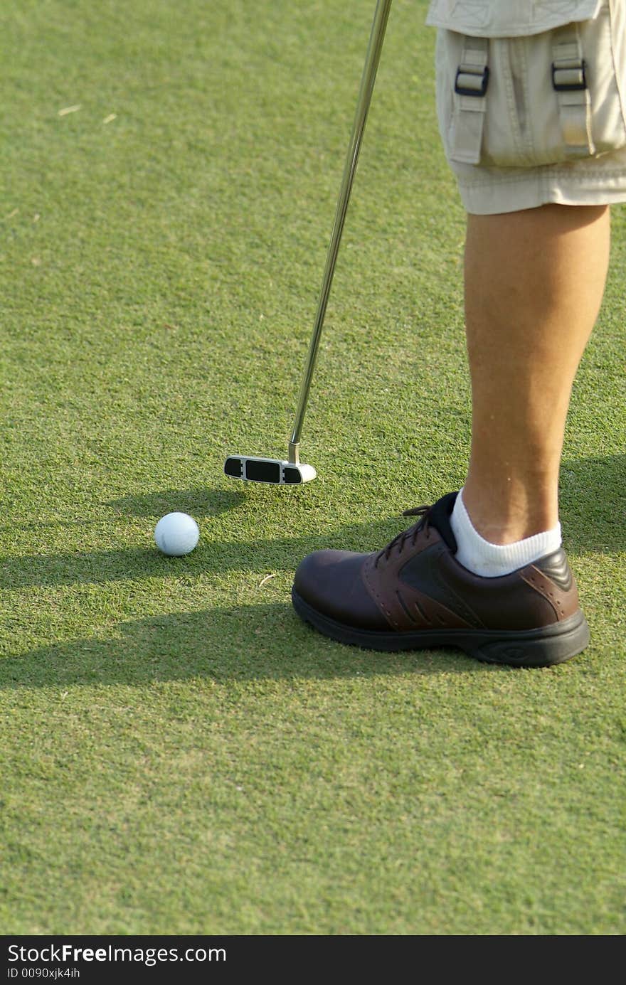 Foot and putter of a man putting on a golf green. The ball has motion blur. Focus on the club-head. Foot and putter of a man putting on a golf green. The ball has motion blur. Focus on the club-head.