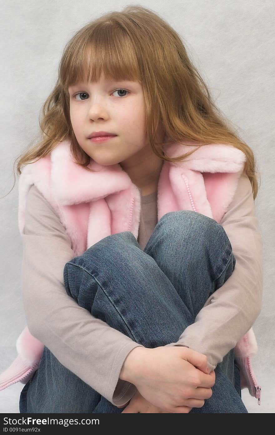 Young girl sits. She wears T-shirt, pink vest and jeans. Young girl sits. She wears T-shirt, pink vest and jeans.