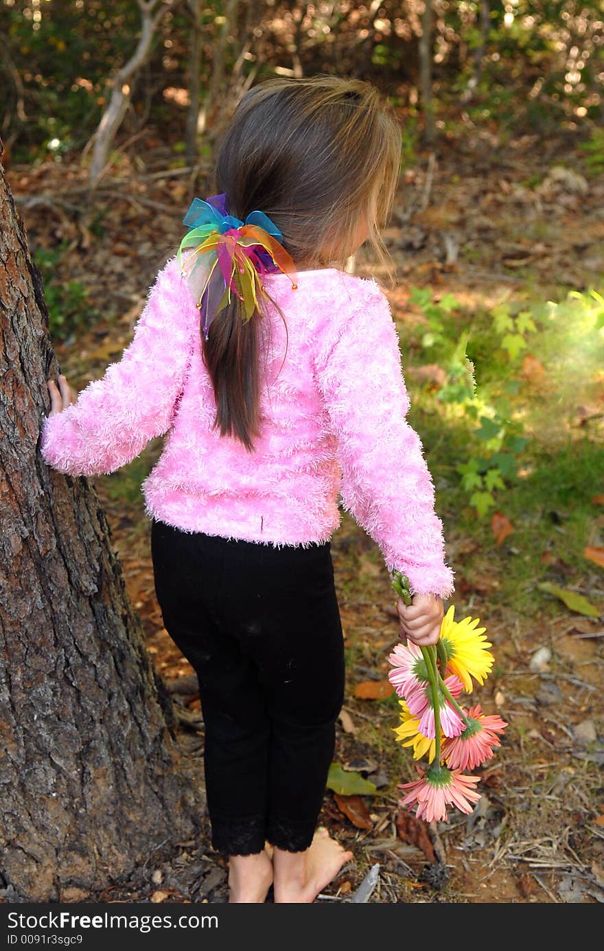 A little girl standing by a tree barefoot holding a bouquet of daisies she just picked from the garden. A little girl standing by a tree barefoot holding a bouquet of daisies she just picked from the garden.