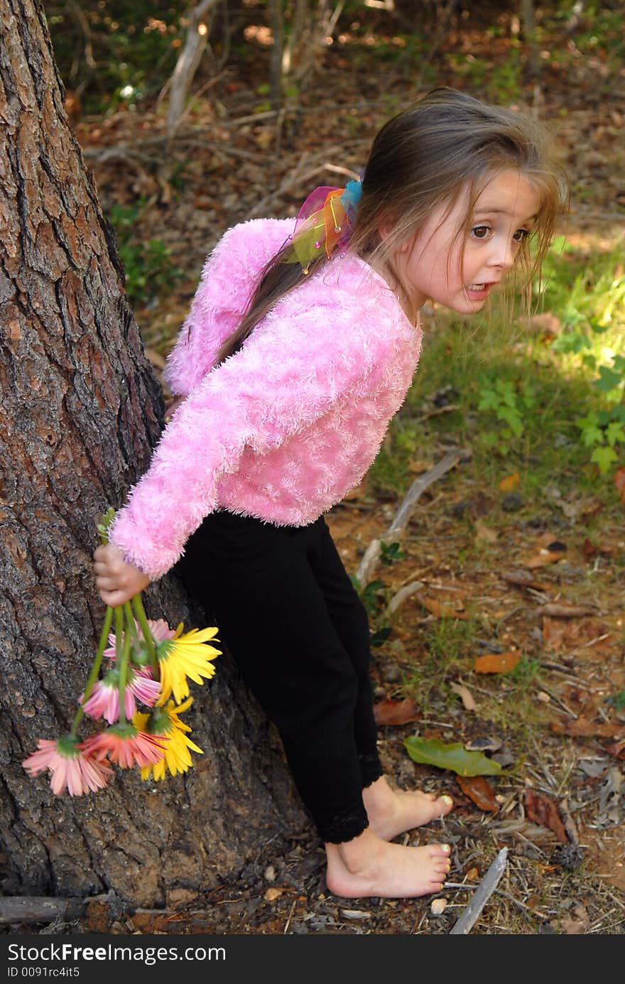 A little girl standing by a tree barefoot holding a bouquet of daisies she just picked from the garden. A little girl standing by a tree barefoot holding a bouquet of daisies she just picked from the garden.