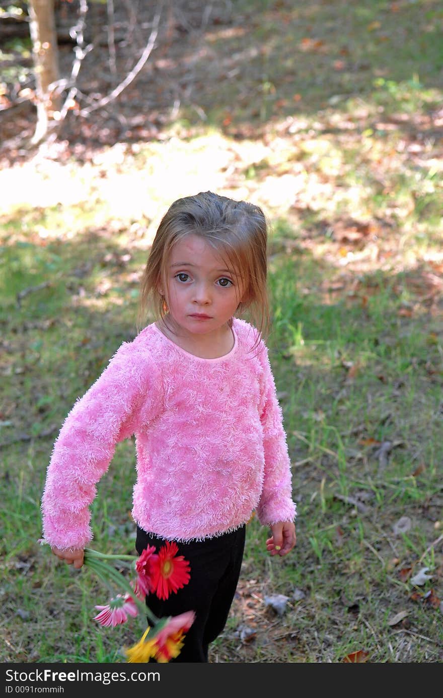 A little girl  holding a bouquet of daisies she just picked from the garden not looking too happy. A little girl  holding a bouquet of daisies she just picked from the garden not looking too happy.