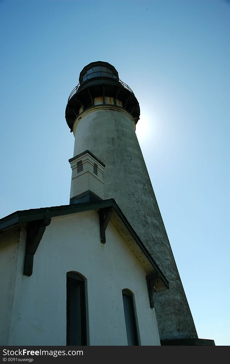 Lighthouse from wide perspective angled upward with sun glowing from behind the top of the lighthouse. Lighthouse from wide perspective angled upward with sun glowing from behind the top of the lighthouse