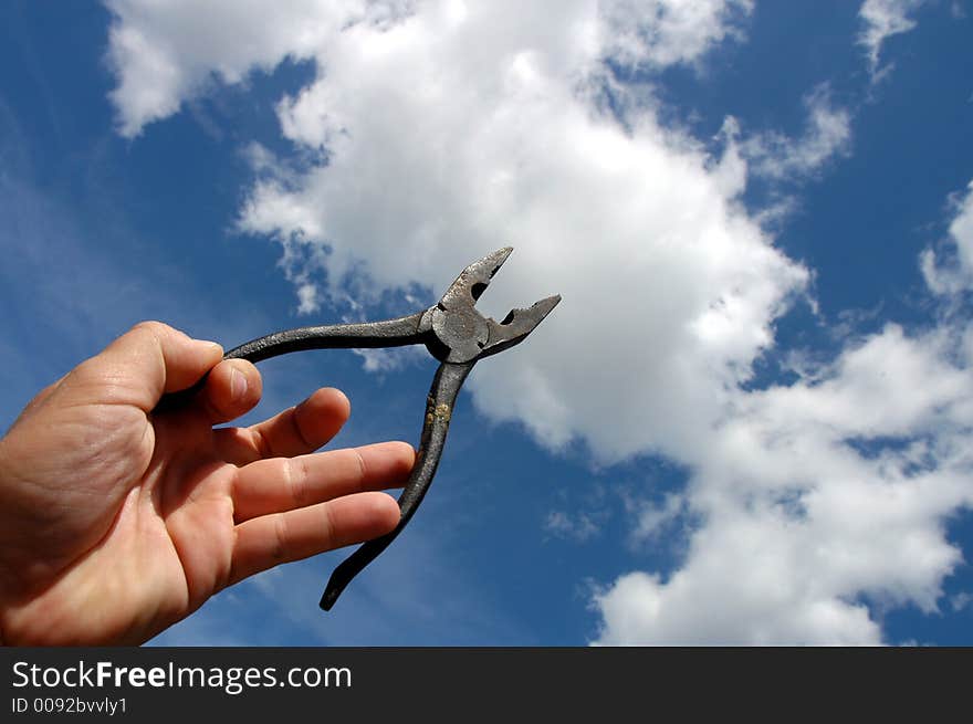 Man holding pliers against a blue sky with clouds.