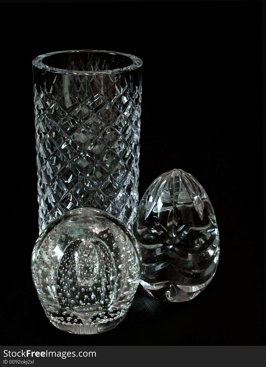 Three crystal objects, a herringbone cut vase, a suspended bubble paperweight and a cut crystal egg isolated on a black background