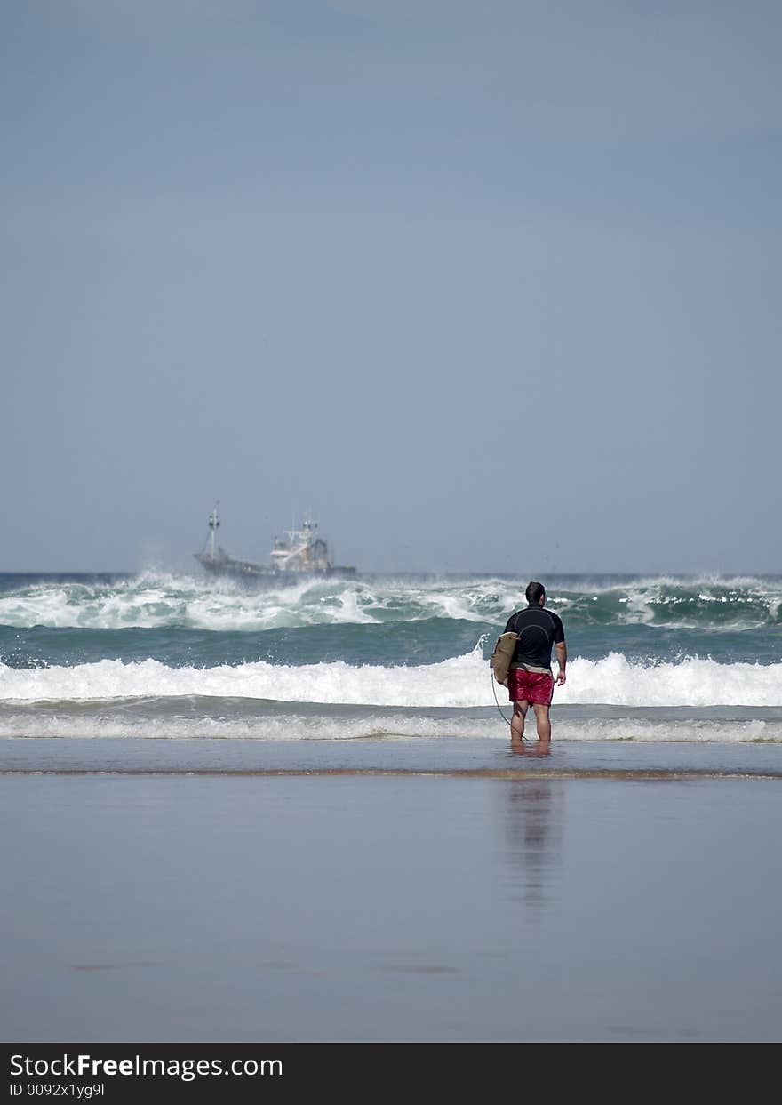 A young man stands on the coastline checking surf conditions