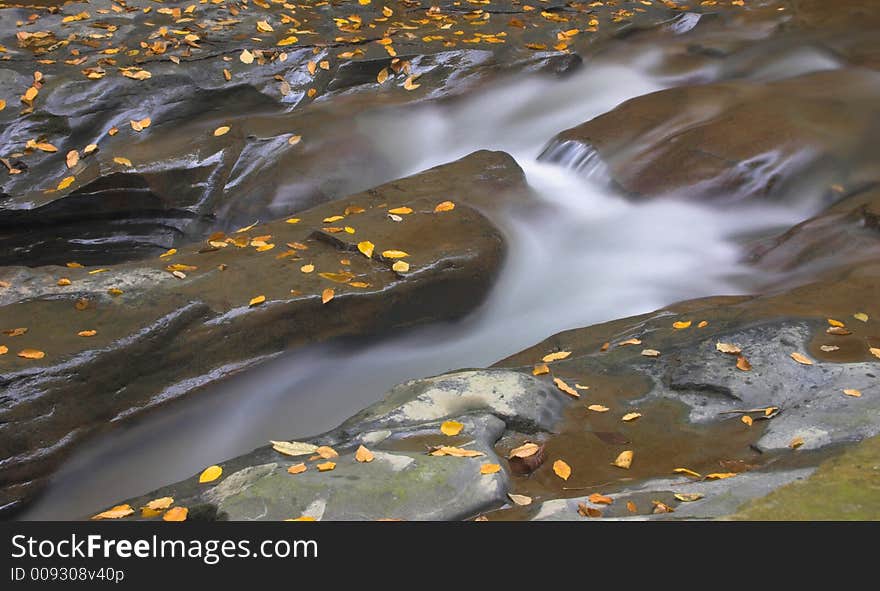 Rocks with autumn leaves and water flowing by. Rocks with autumn leaves and water flowing by