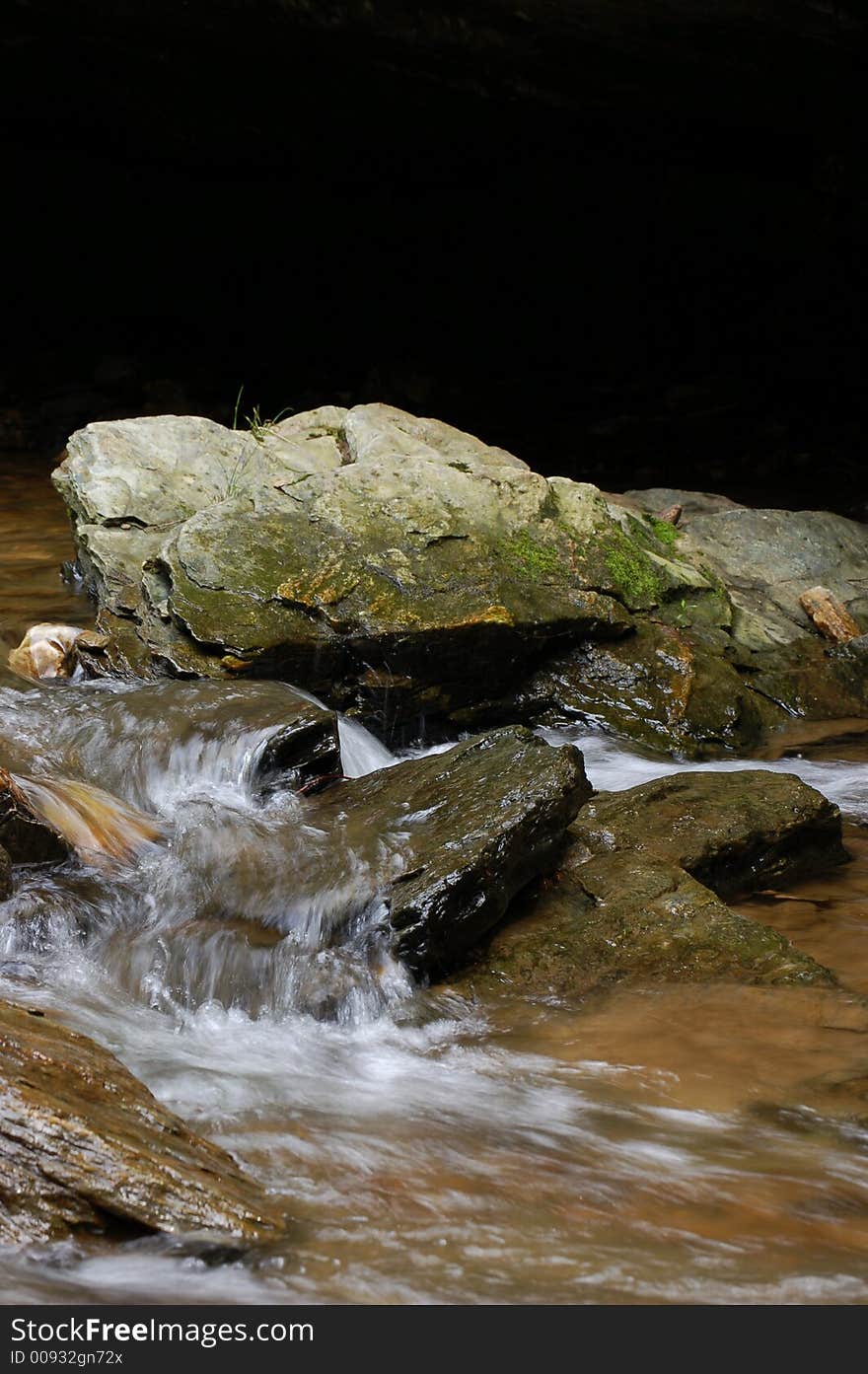 Top third of photo in deep natural shadow for copy, focus on boulder in center, waterfall pleasantly blurred through bottom half. Top third of photo in deep natural shadow for copy, focus on boulder in center, waterfall pleasantly blurred through bottom half.