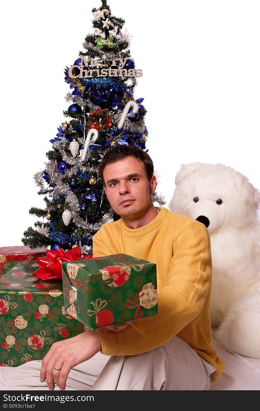 A handsome guy sits under the christmas tree giving you a gift. A handsome guy sits under the christmas tree giving you a gift