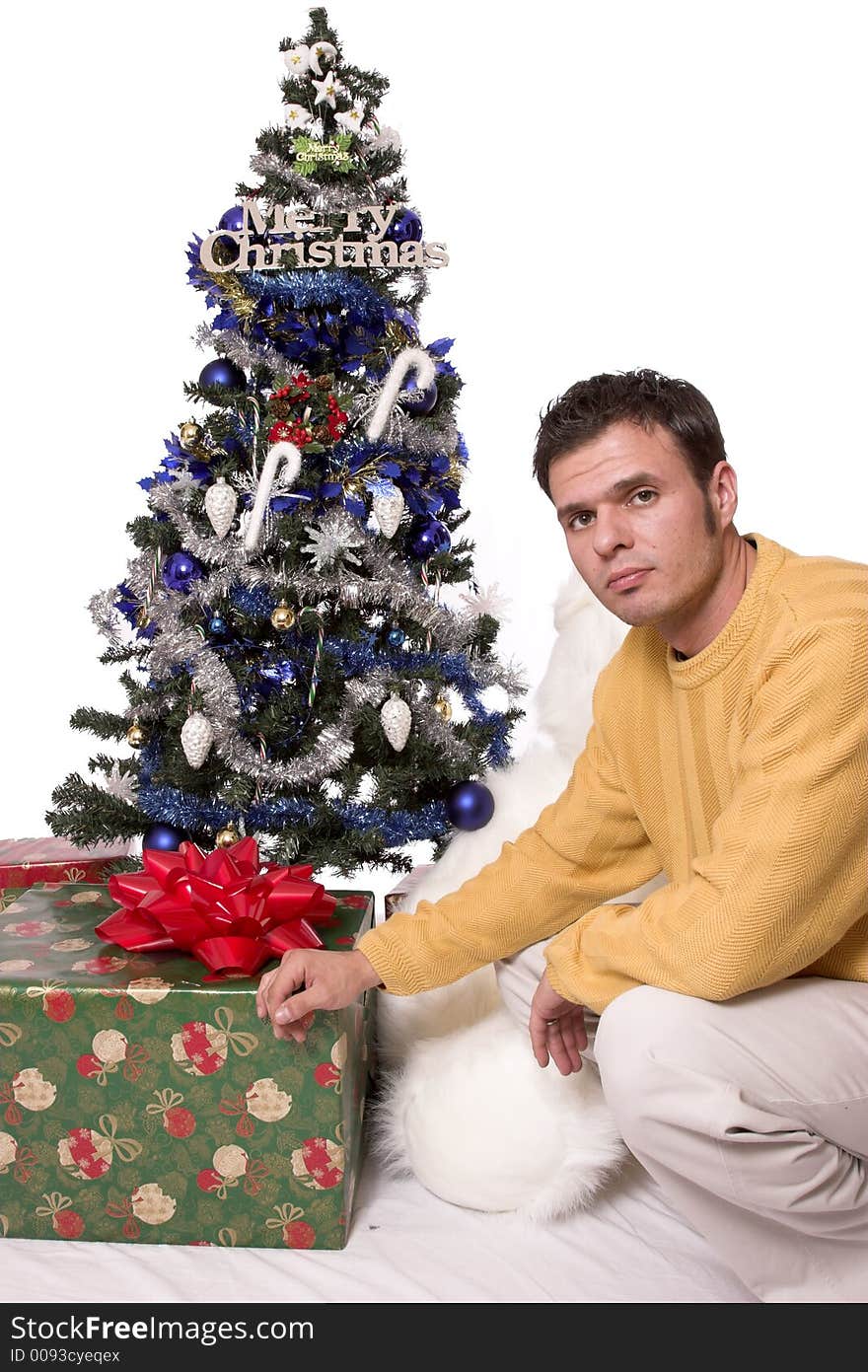 A handsome guy sits under the christmas tree giving you a gift. A handsome guy sits under the christmas tree giving you a gift