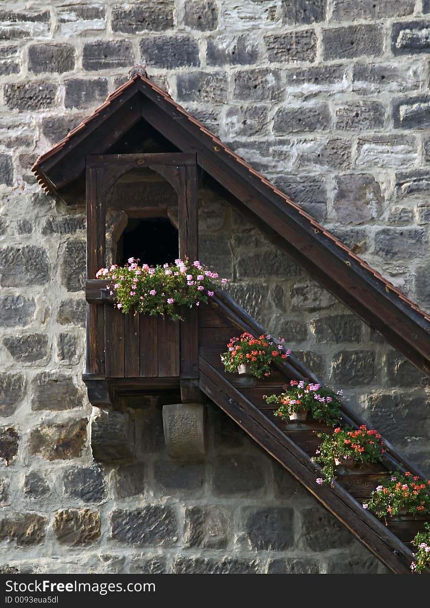 Entrance to a medieval tower with roof covered stairs which are decorated with flower boxes