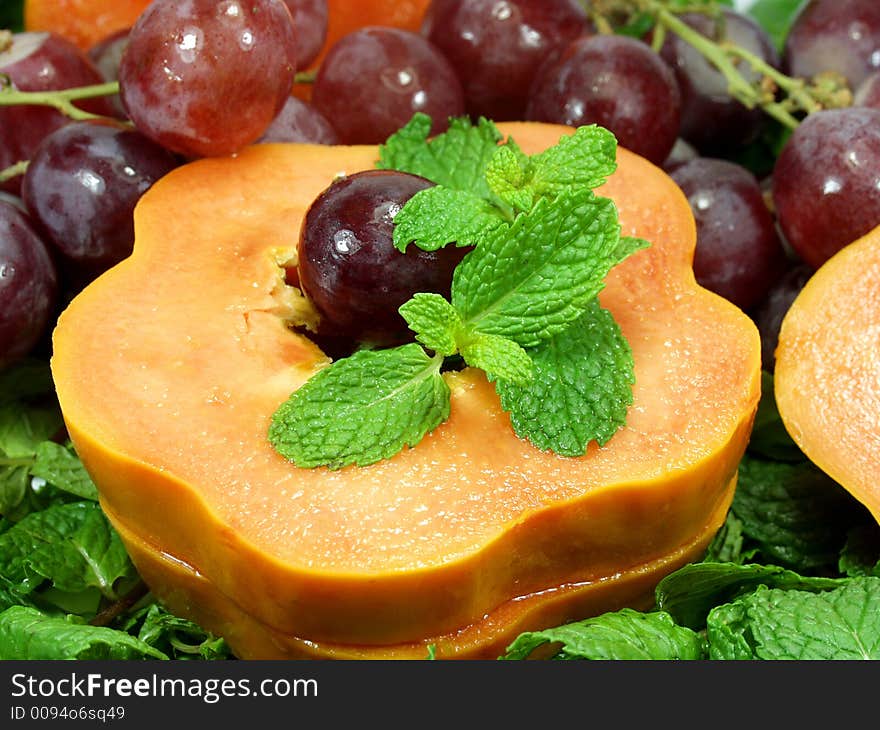 Close up of papaya slices whit red grapes and mint leaves. Close up of papaya slices whit red grapes and mint leaves