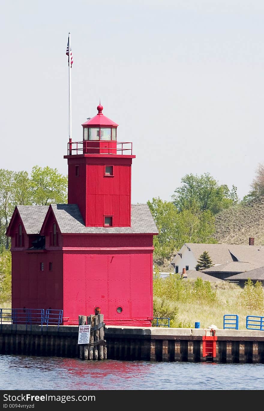 An old red lighthouse at the end of a pier on a lake shore