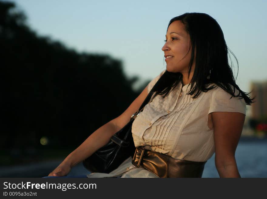 Pretty girl carrying a purse enjoying sunset at park with sunset ray shine over her face. Pretty girl carrying a purse enjoying sunset at park with sunset ray shine over her face