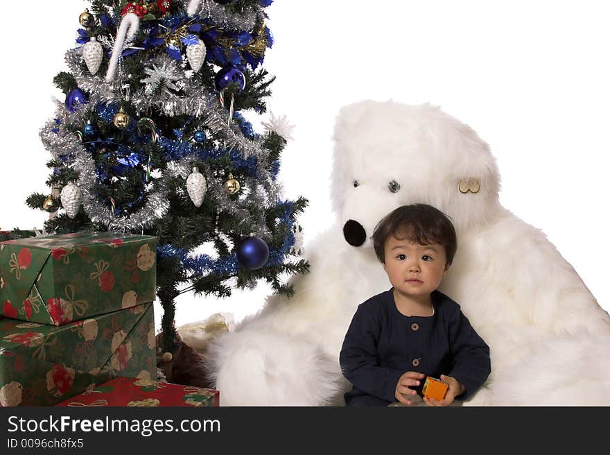 A little boy sits between a giant stuffed bears legs, under the christmas tree. A little boy sits between a giant stuffed bears legs, under the christmas tree