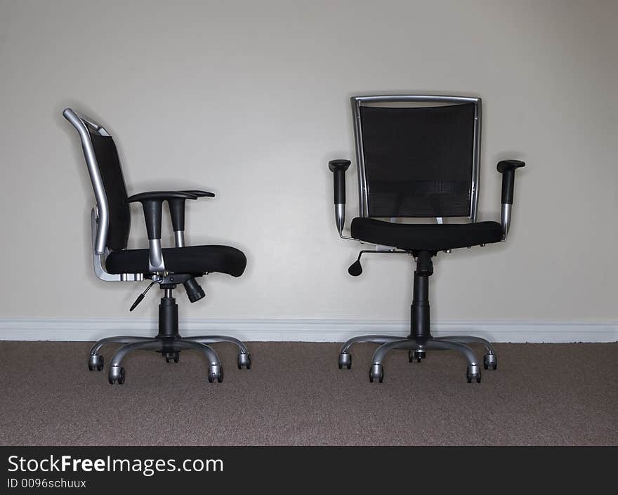 One business chair is facing and looking at the taller, more confident business chair, which is the boss. One business chair is facing and looking at the taller, more confident business chair, which is the boss