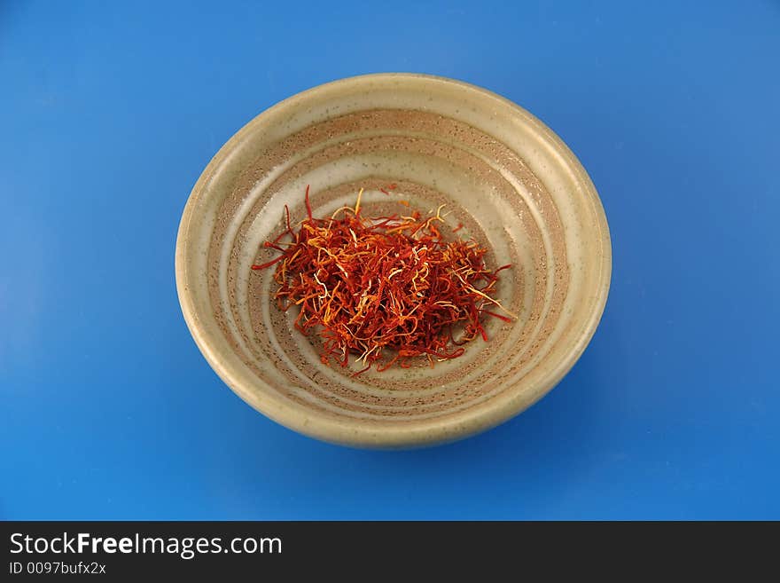 A small dish with the very expensive spice saffron inside on a blue background.