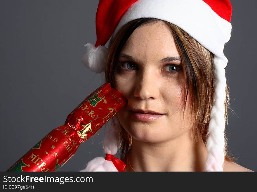 Young santa girl in front of grey background with christmas cracker. Young santa girl in front of grey background with christmas cracker