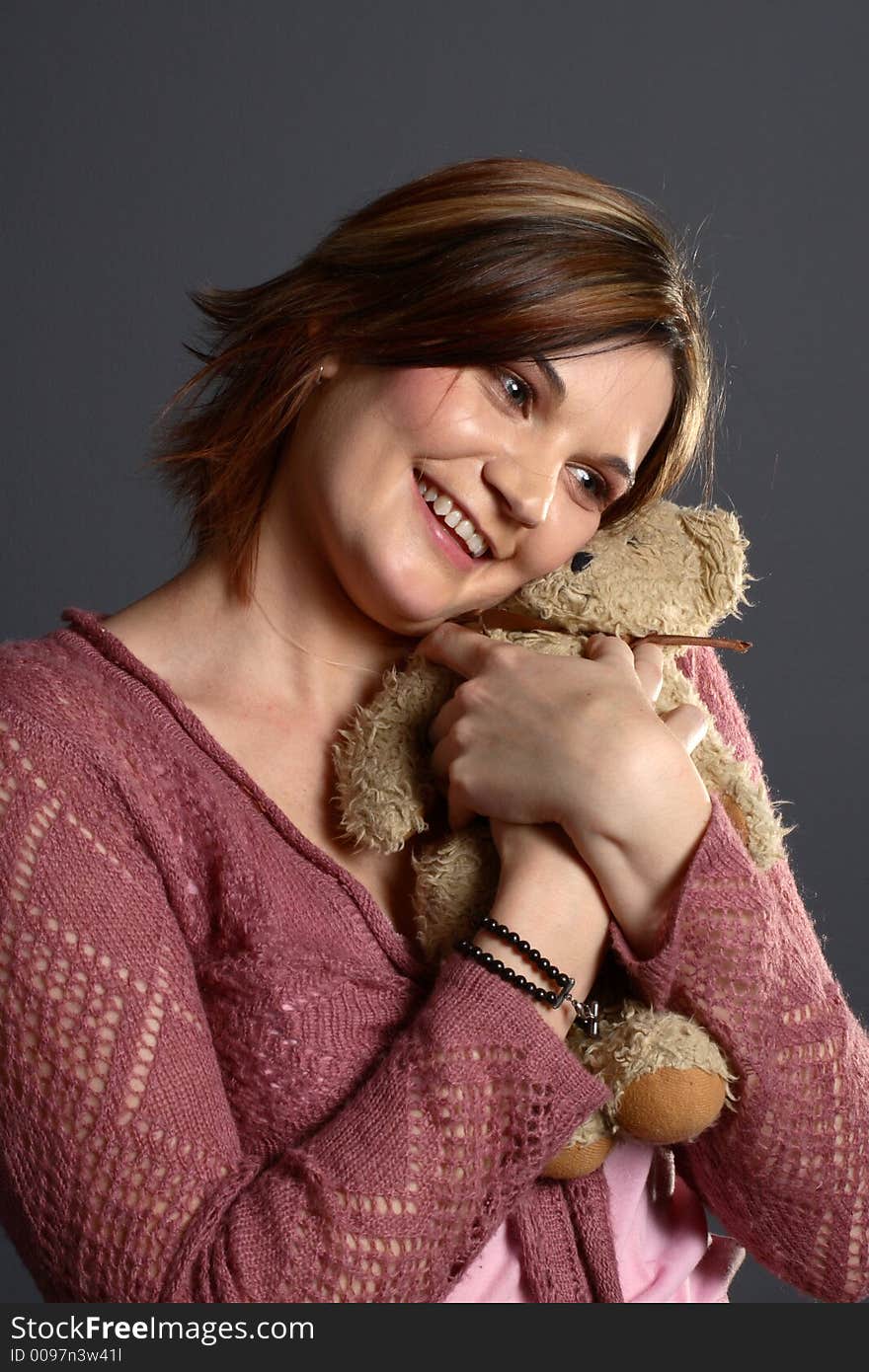 Brunette model hugging traditional teddy bear in front of grey background. Brunette model hugging traditional teddy bear in front of grey background