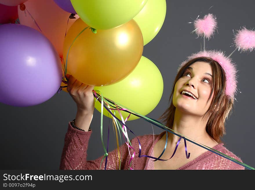 Brunette model with alien antenna and balloons in front of grey background. Brunette model with alien antenna and balloons in front of grey background