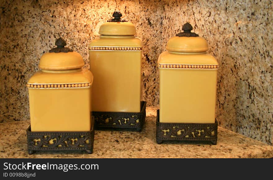 Set of gold-colored cannisters on carved wooden stands sitting on granite cabinet. Set of gold-colored cannisters on carved wooden stands sitting on granite cabinet