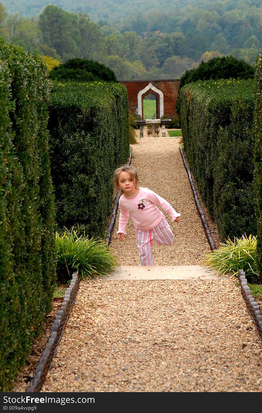 A little girl hopping, skipping and jumping on a path in the garden with a view in the background. A little girl hopping, skipping and jumping on a path in the garden with a view in the background.