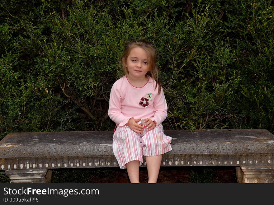 A beautiful little girl dressed in pink sitting on a concrete garden bench. She's wearing flip-flops and has a sweet expression on her face. A beautiful little girl dressed in pink sitting on a concrete garden bench. She's wearing flip-flops and has a sweet expression on her face.