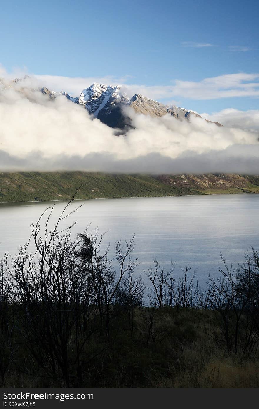 Cloudy snow mountain and lake at New Zealand, framed with dry trees. Cloudy snow mountain and lake at New Zealand, framed with dry trees.