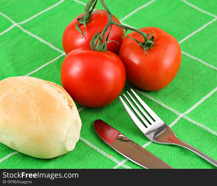 Red tomatoes on vine presented on green cloth with fresh bread and cuttlery. Red tomatoes on vine presented on green cloth with fresh bread and cuttlery