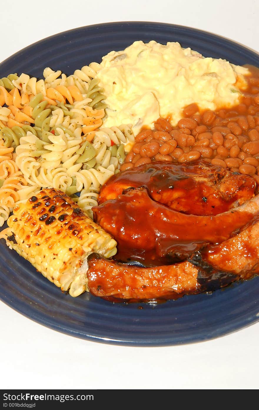 Spare ribs corn potato and pasta salad and baked beans on a dinner plate. Spare ribs corn potato and pasta salad and baked beans on a dinner plate