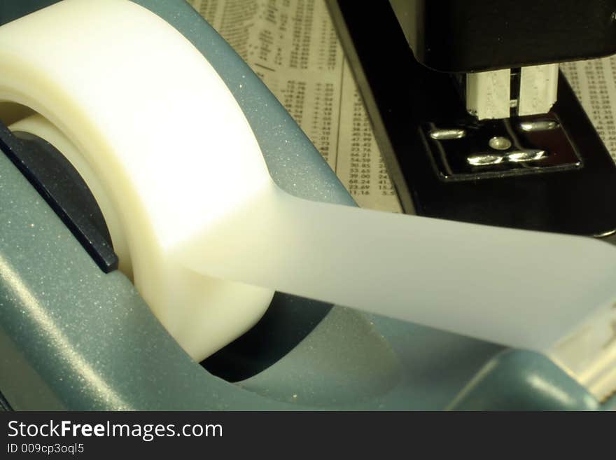 This is a close up image of a stapler and tape dispenser on a newspaper. This is a close up image of a stapler and tape dispenser on a newspaper.