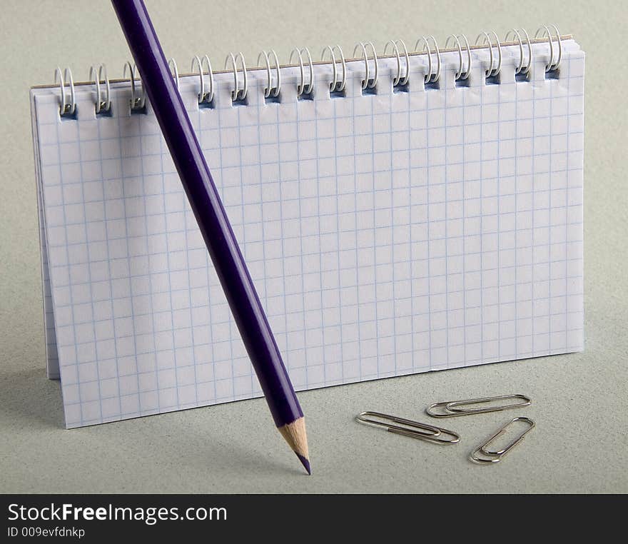 Notebook in a cell with a dark blue pencil and clips for a paper. Notebook in a cell with a dark blue pencil and clips for a paper