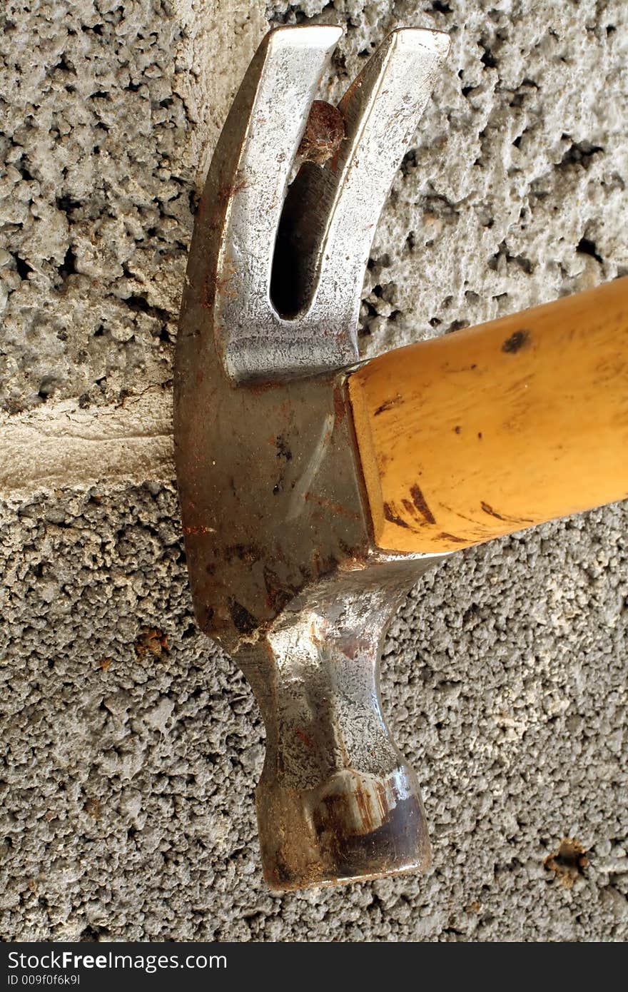 This is a close up image of a hammer pulling a nail out of a cinder block wall. This is a close up image of a hammer pulling a nail out of a cinder block wall.