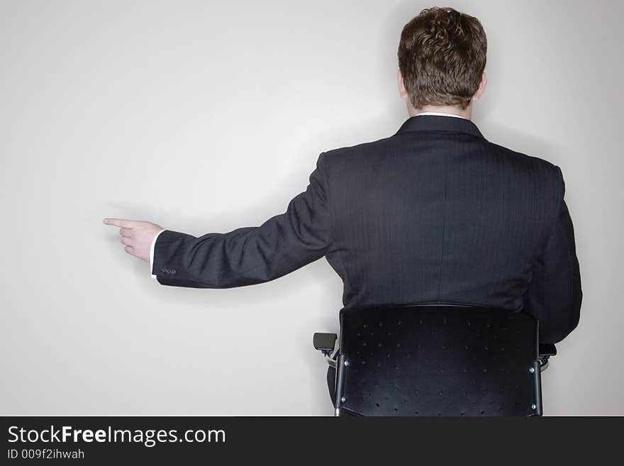 Businessman sitting and pointing in his office chair with a white background and a rear view