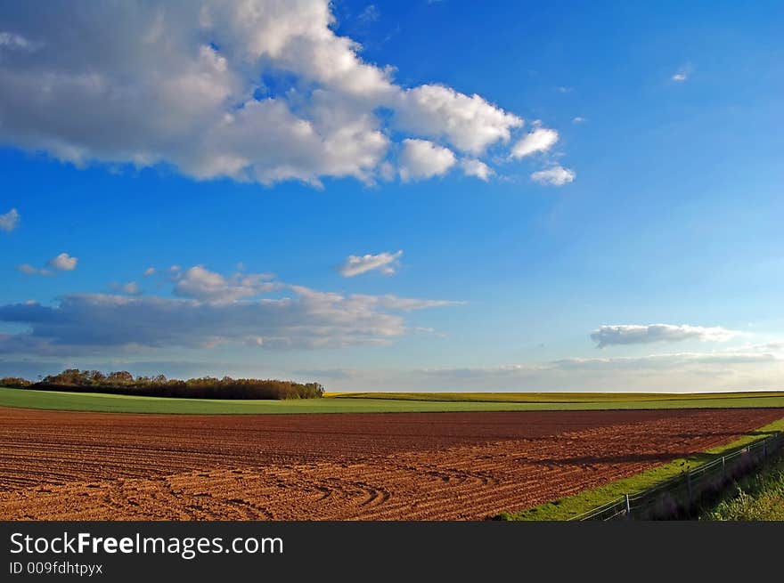 A field was just ploughed, with green corn fields and a woodland in the background. A field was just ploughed, with green corn fields and a woodland in the background.