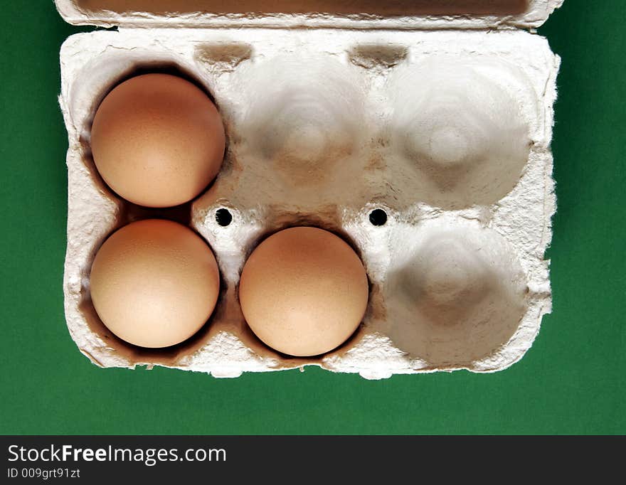 Three Brown Eggs In A Grey Cardboard Box On Green Background. Three Brown Eggs In A Grey Cardboard Box On Green Background