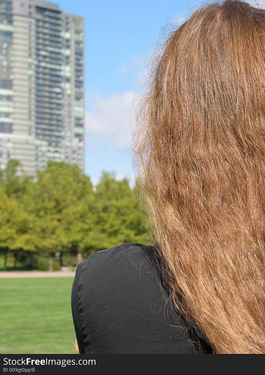 A young woman looks at a high-rise building looming over a city park. A young woman looks at a high-rise building looming over a city park.