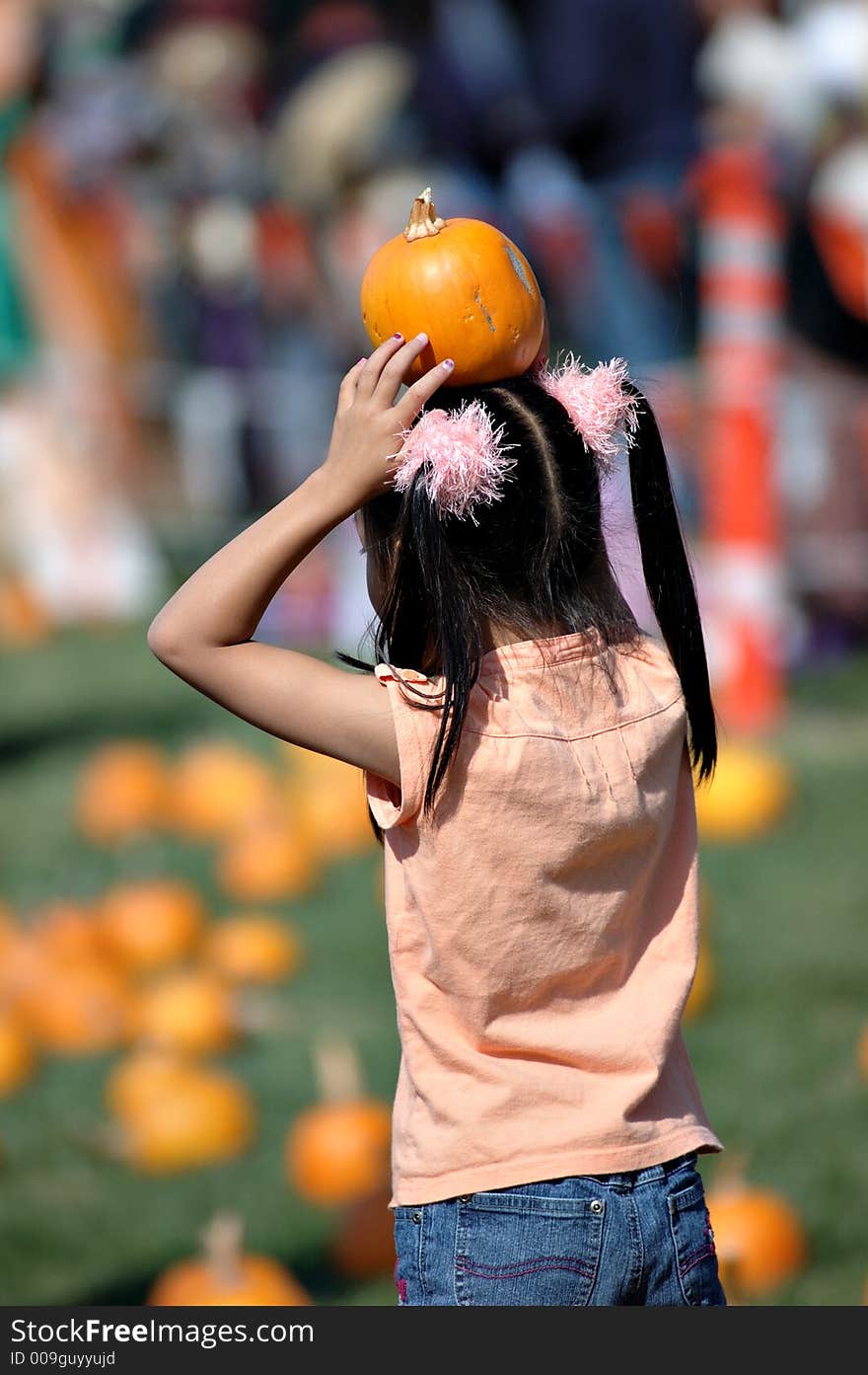 A little holding a small pumpkin on her head.  picture showing her back. A little holding a small pumpkin on her head.  picture showing her back.