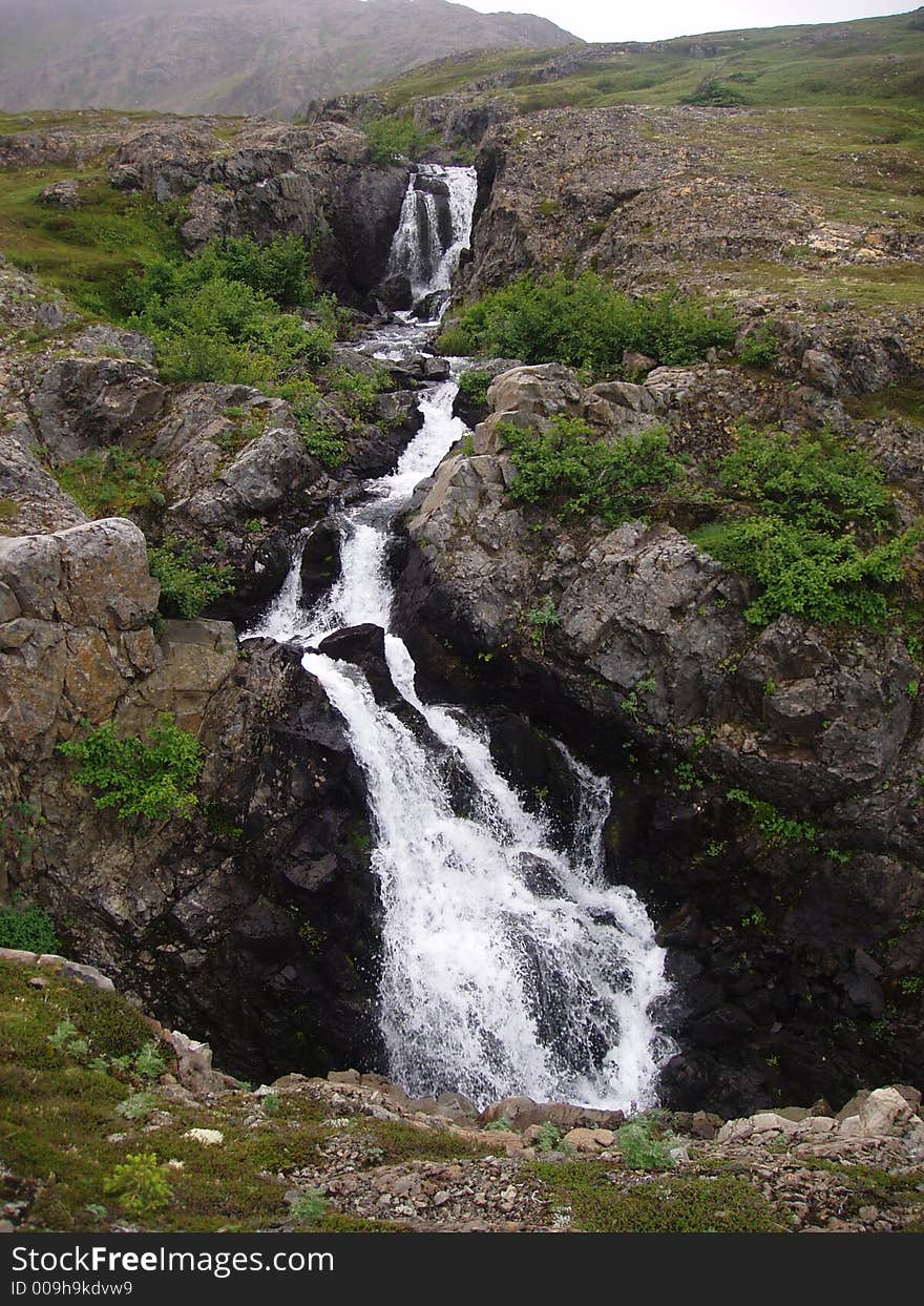 Alpine waterfall gushing down rock crevice in alaska